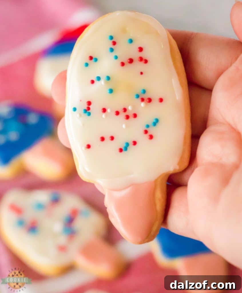 Assortment of colorful popsicle sugar cookies decorated with sprinkles, laid out on a baking sheet.