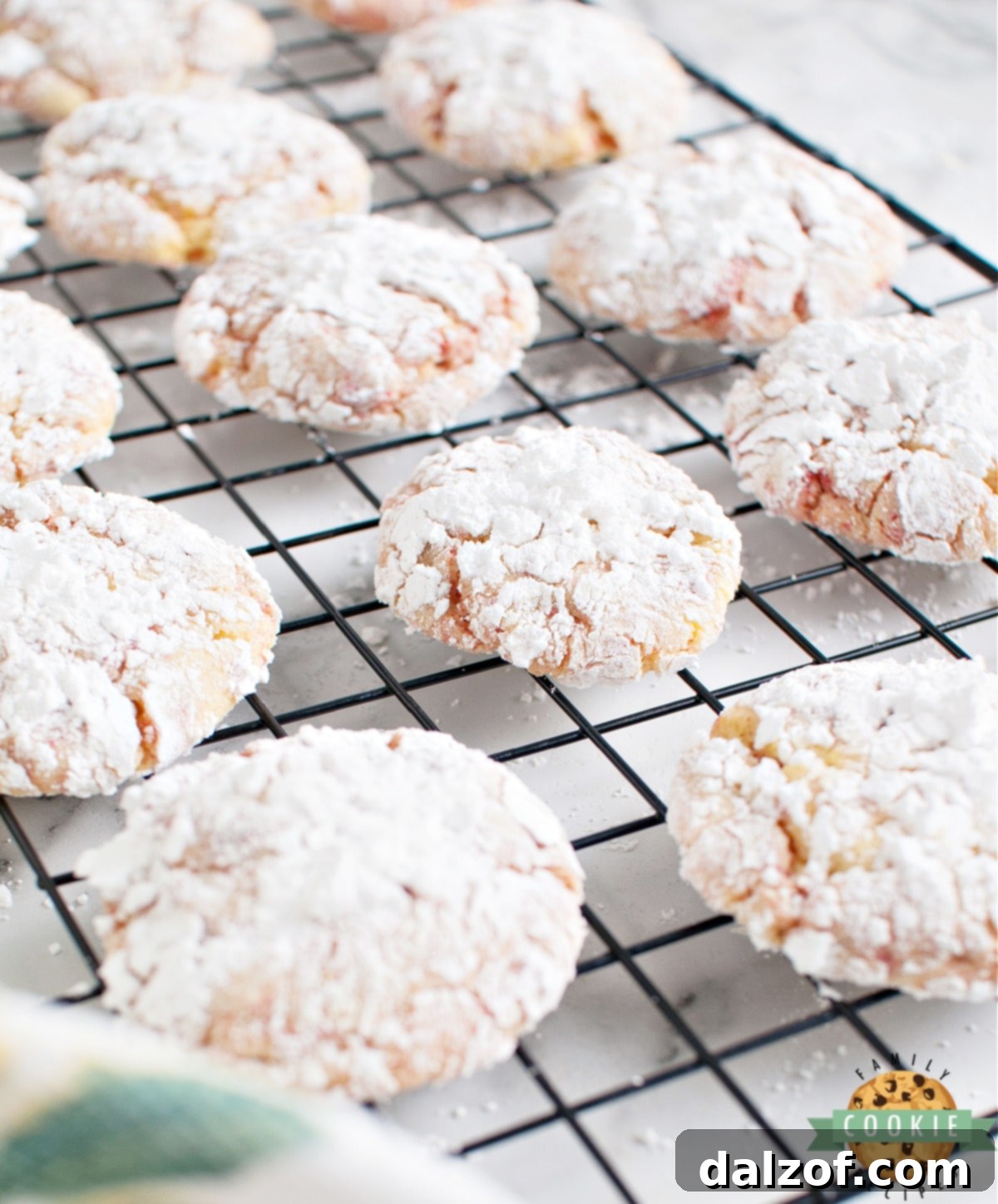 A batch of freshly baked Lemon Cake Mix Crinkle Cookies with prominent red specks from freeze dried strawberries, arranged on a cooling rack.