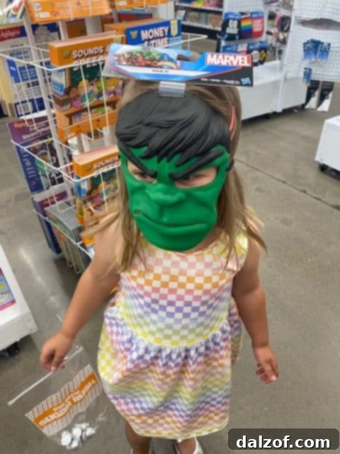 A little girl wearing an oversized Hulk mask in a store, a humorous and endearing moment.