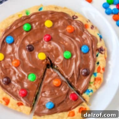 A perfectly baked M&M Cookie Pizza topped with melted chocolate and colorful candies.