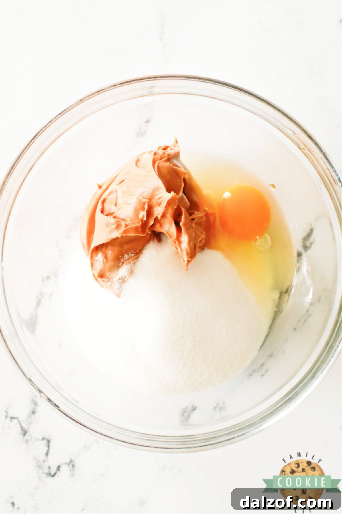 A mixing bowl with peanut butter, sugar, and an egg, partially mixed together, showing the creamy texture starting to form.