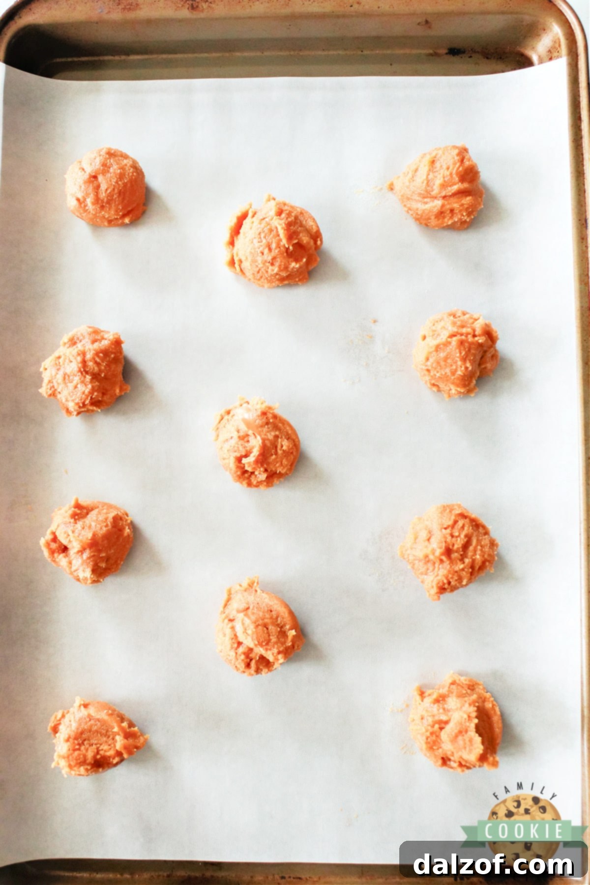 Scoops of peanut butter cookie dough neatly arranged on a parchment-lined baking sheet.