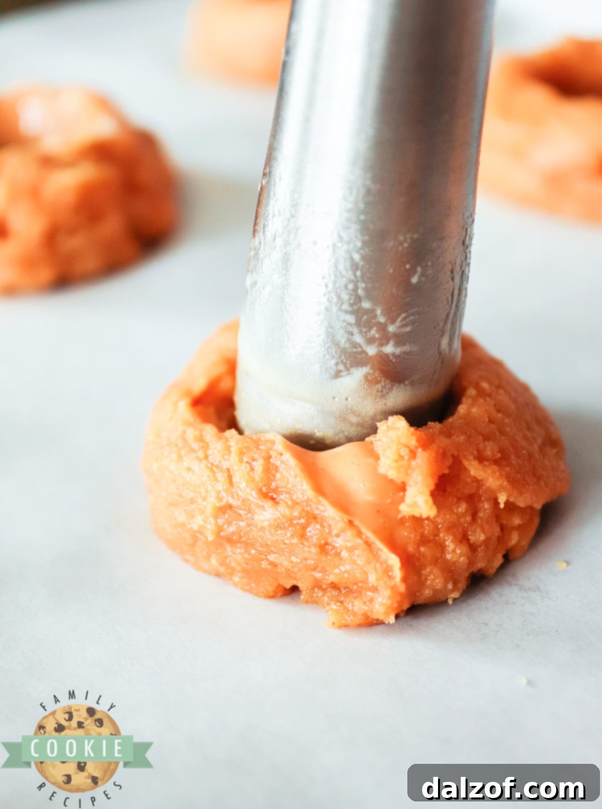 A small measuring spoon creating an indentation in a scooped peanut butter cookie dough ball.