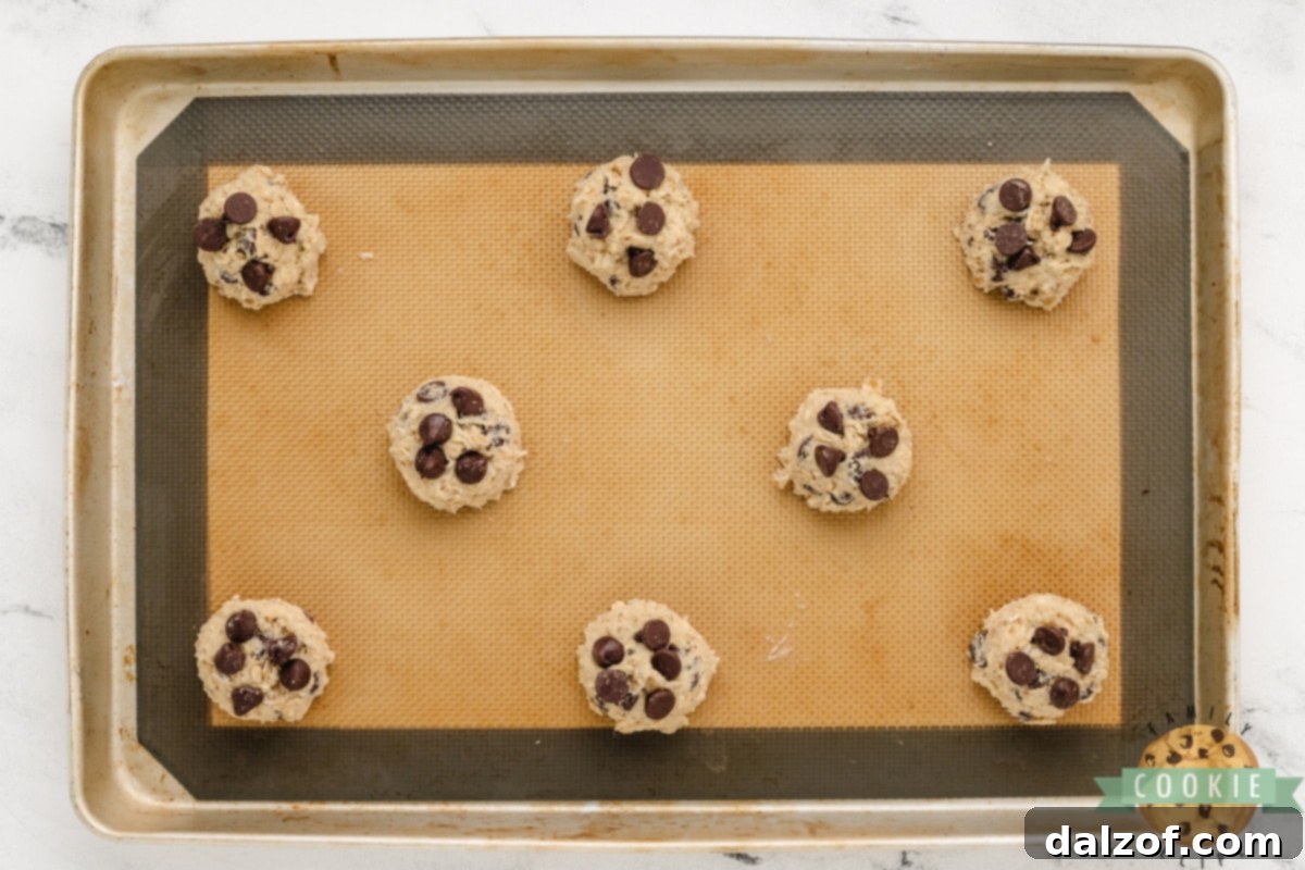 Scooping oatmeal chocolate chip cookie dough onto a baking sheet.