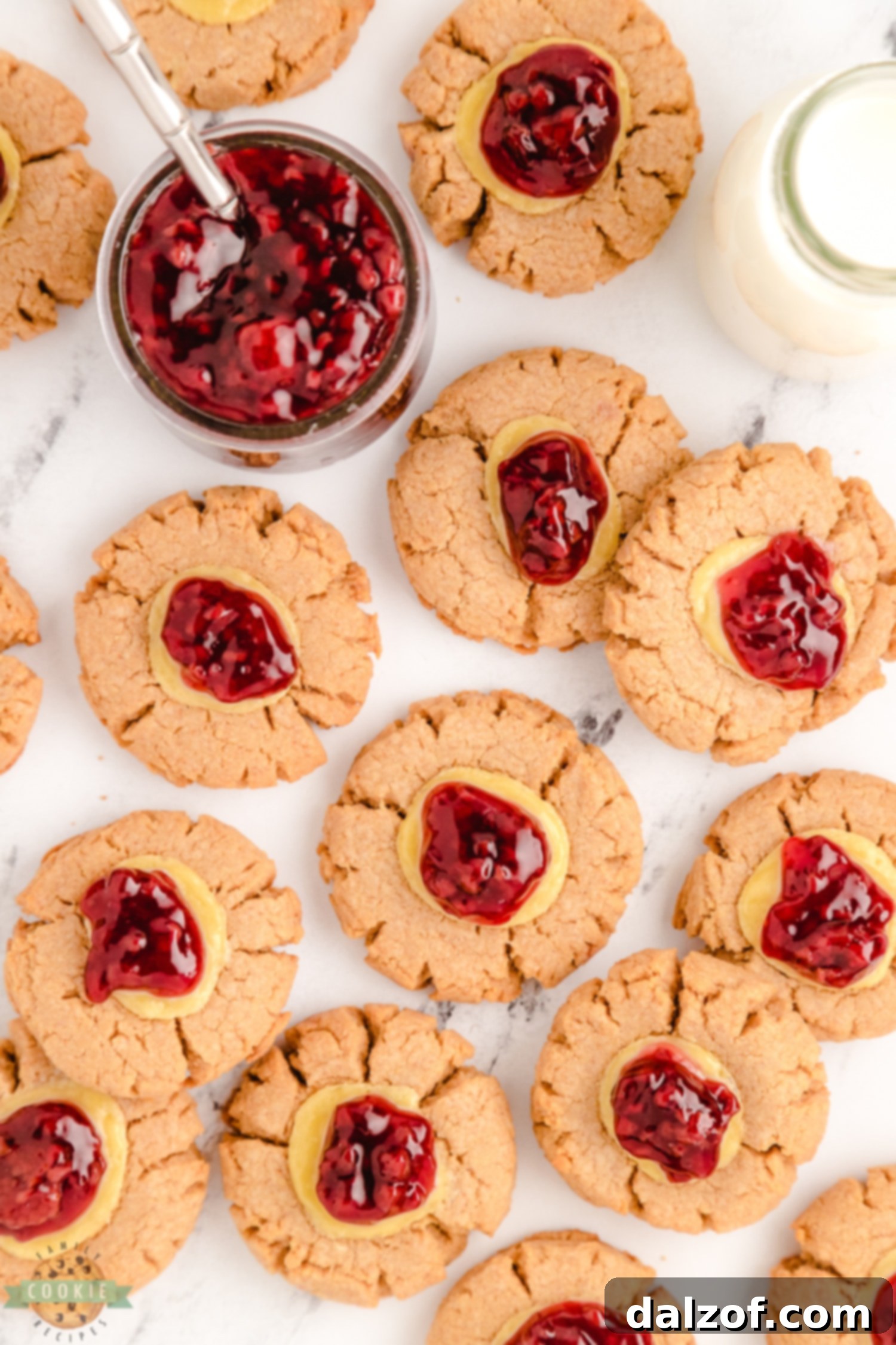 Close-up of raspberry pie filling being spooned onto the creamy cheesecake center of freshly baked cookies.
