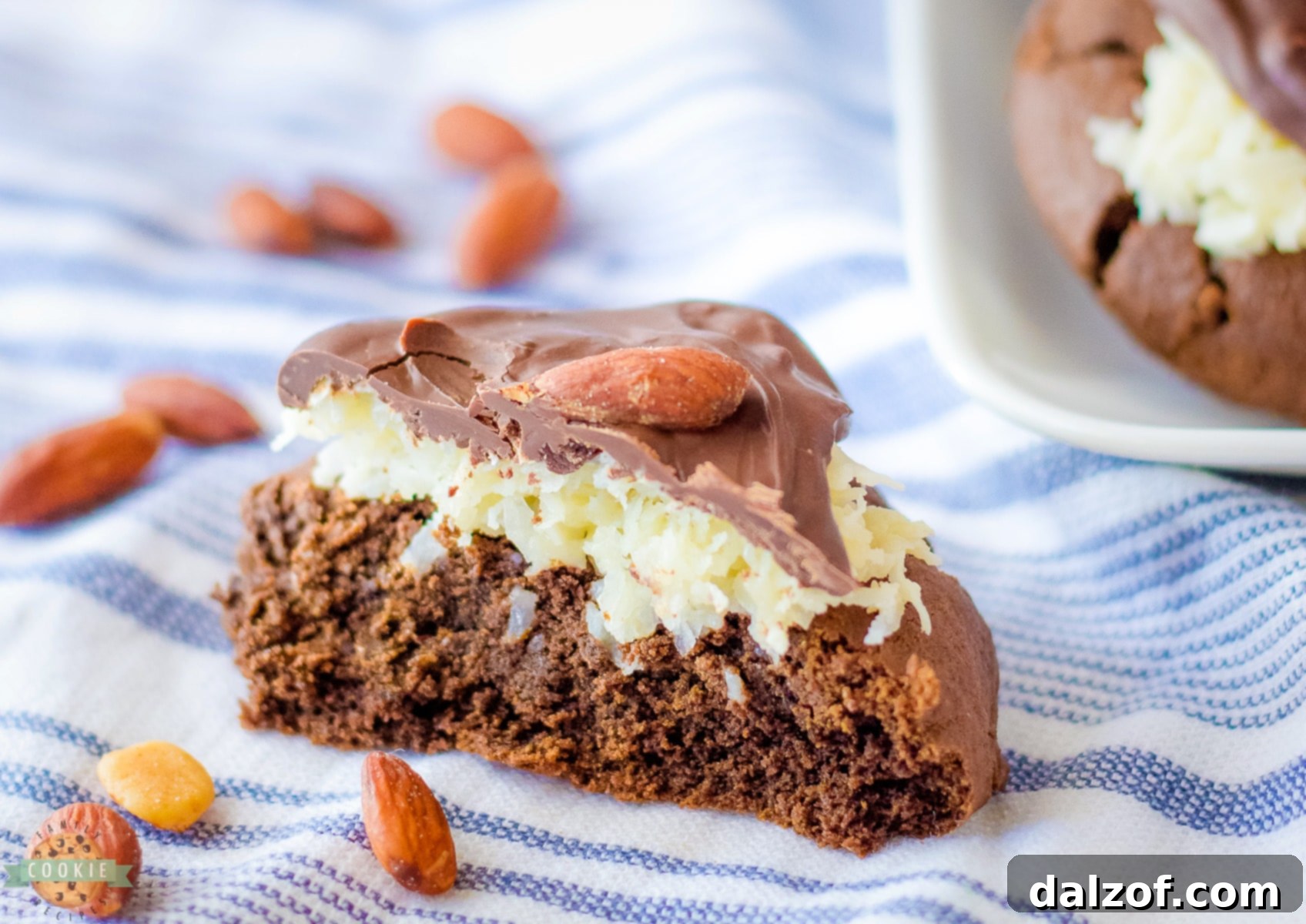 A Bakery Style Almond Joy Cookie cut in half, showing the layers of chocolate cookie, coconut, and chocolate almond topping