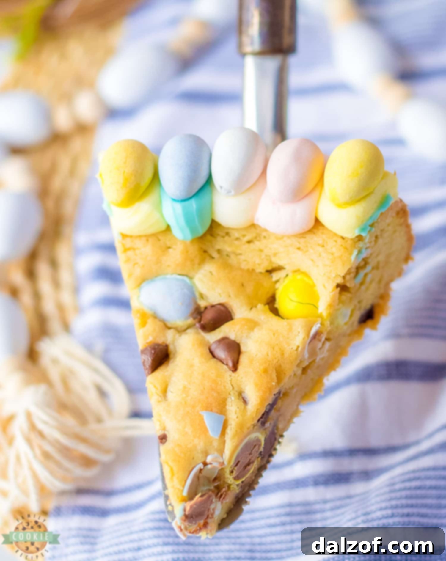 A perfectly sliced portion of Easter cookie cake, revealing its soft, chewy interior studded with chocolate chips and mini Cadbury eggs, ready to be enjoyed.