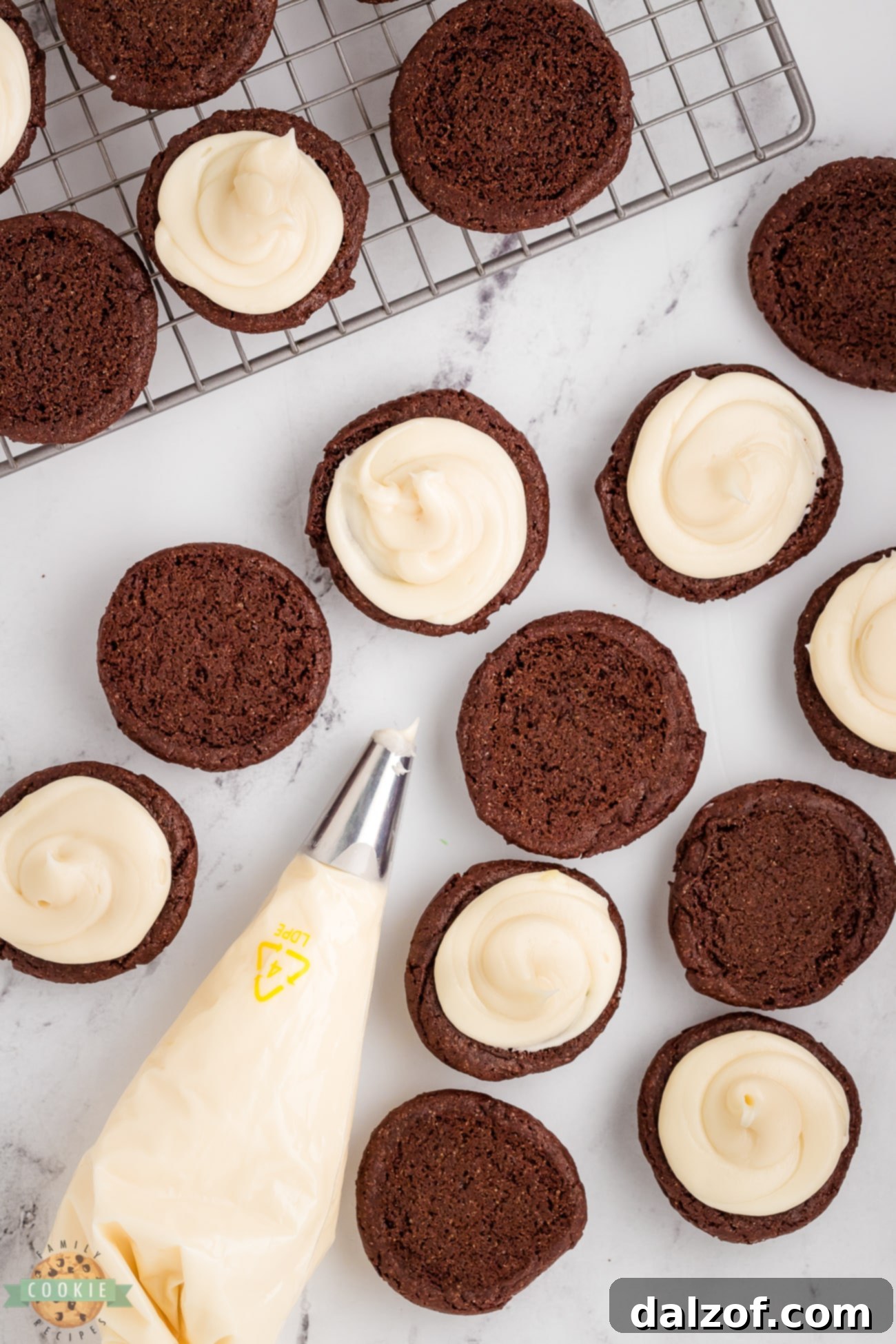 Hands carefully adding creamy white cream cheese frosting to the bottom of a homemade chocolate cookie, preparing an Oreo sandwich
