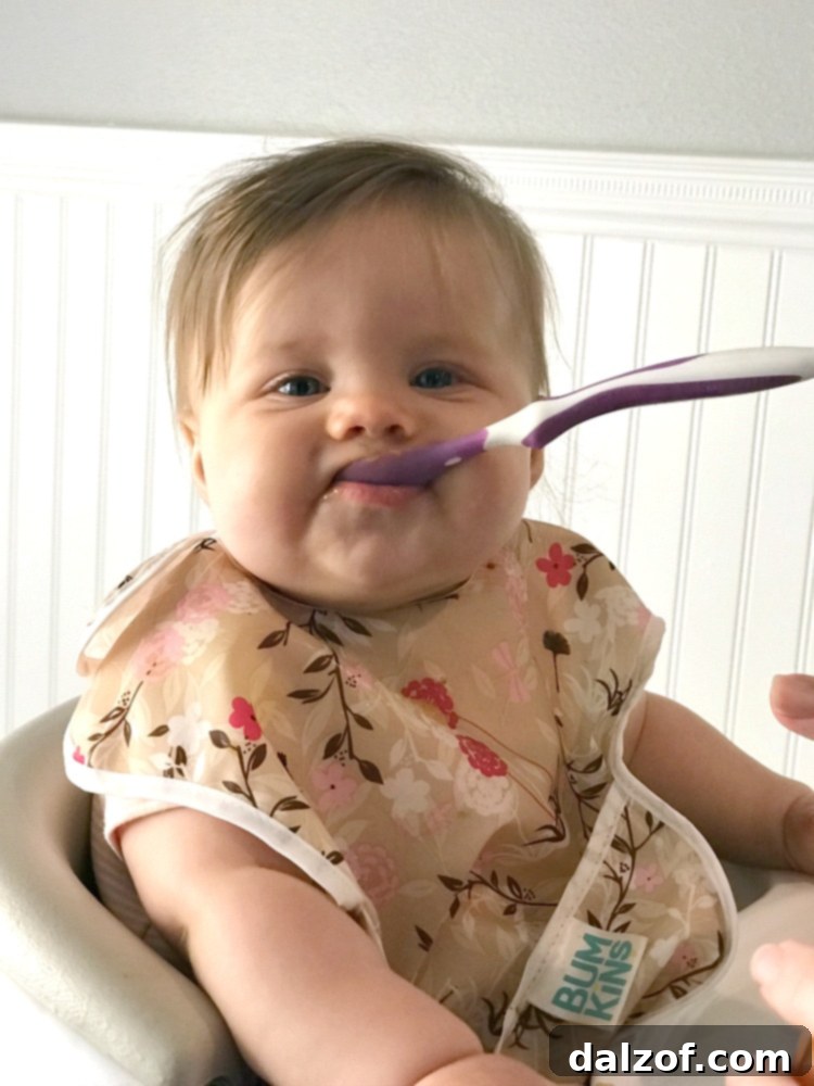 A baby smiling, wearing a cute outfit, likely enjoying a meal