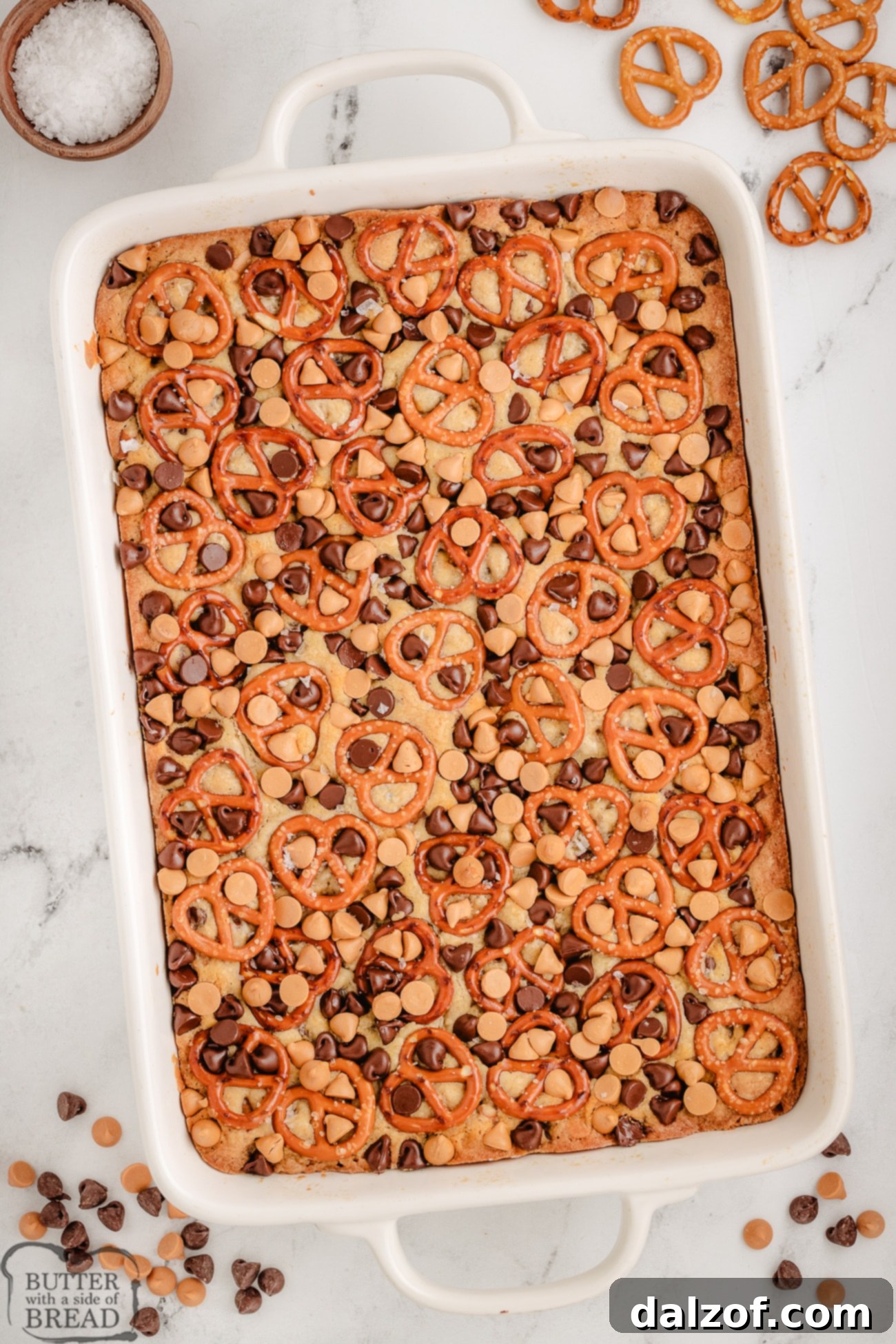 A pan filled with cookie bar dough made with butterscotch chips and pretzels, ready for baking.