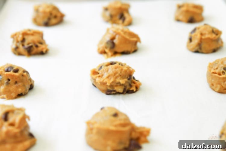 Scooping soft pumpkin chocolate chip cookie dough onto a baking sheet, ready for the oven.