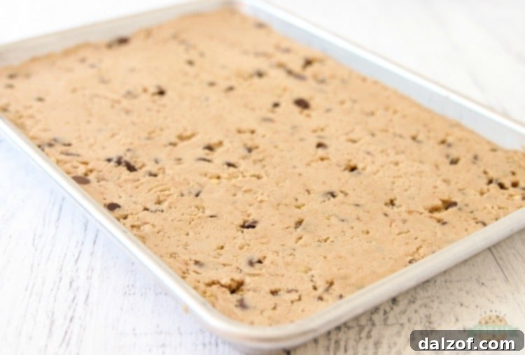 Chocolate chip cookie dough being pressed into a parchment-lined baking pan