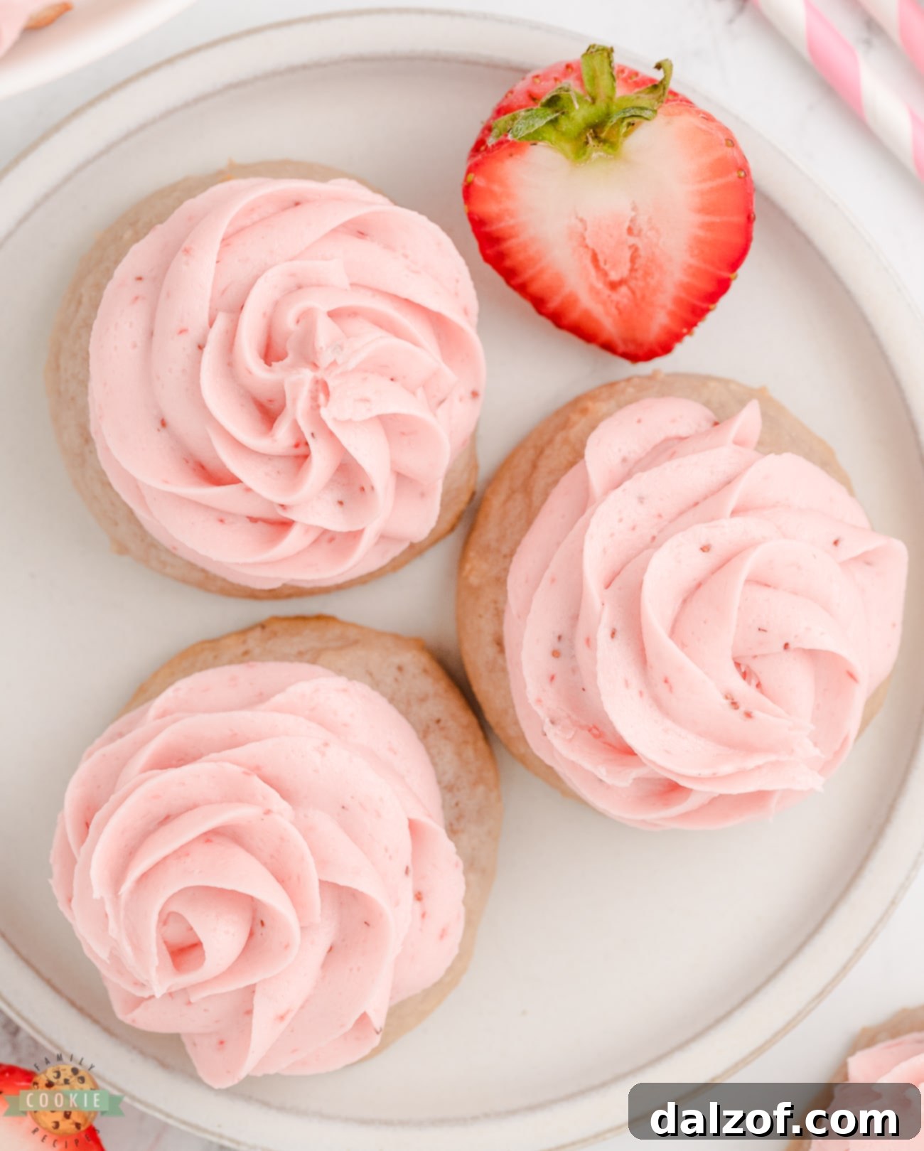 Sweet Frosted Strawberry Cookies 2 Three frosted strawberry cookies on a plate, showcasing their soft texture and vibrant pink frosting.