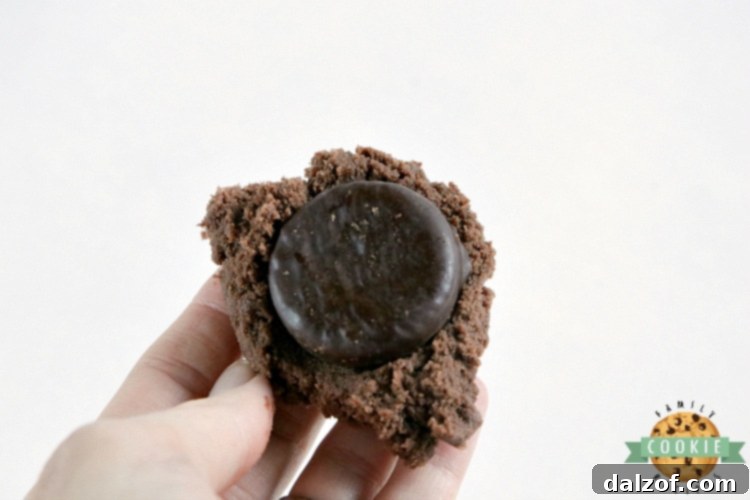 Hands pressing cookie dough around a York peppermint patty on a baking sheet.