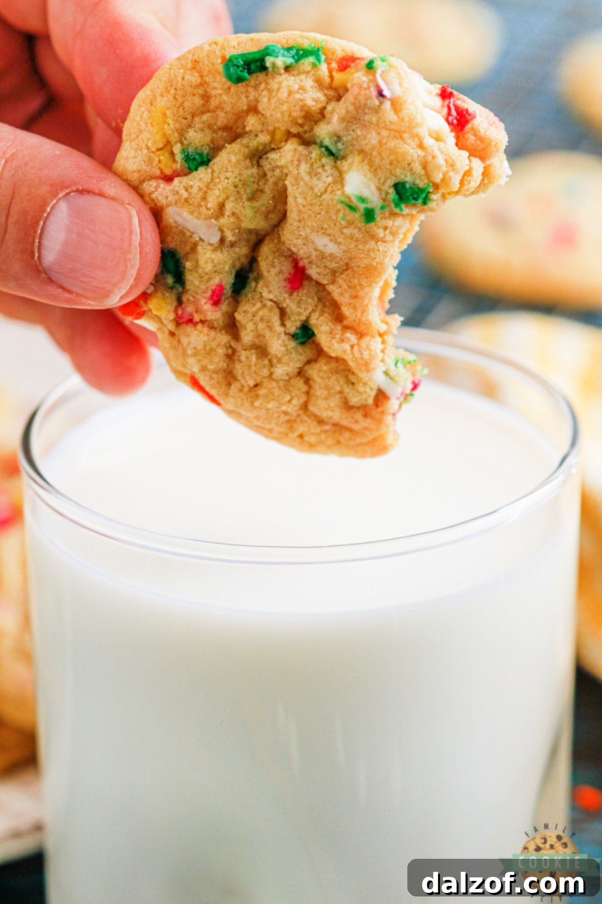 A warm, soft Funfetti cookie being dipped into a cold glass of milk, highlighting its perfect texture.
