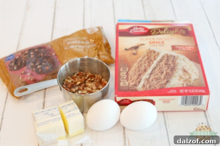 Ingredients for making spice cake mix cookies laid out on a table, including cake mix, eggs, butter, caramel chips, and pecans.