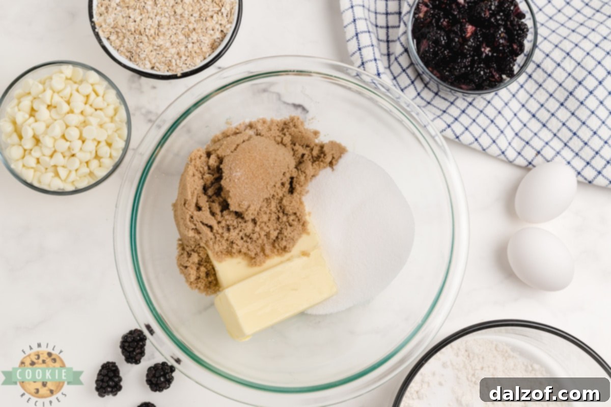 A bowl of fresh blackberries, a bowl of quick oats, and a bowl of white chocolate chips, key ingredients for the cookies.