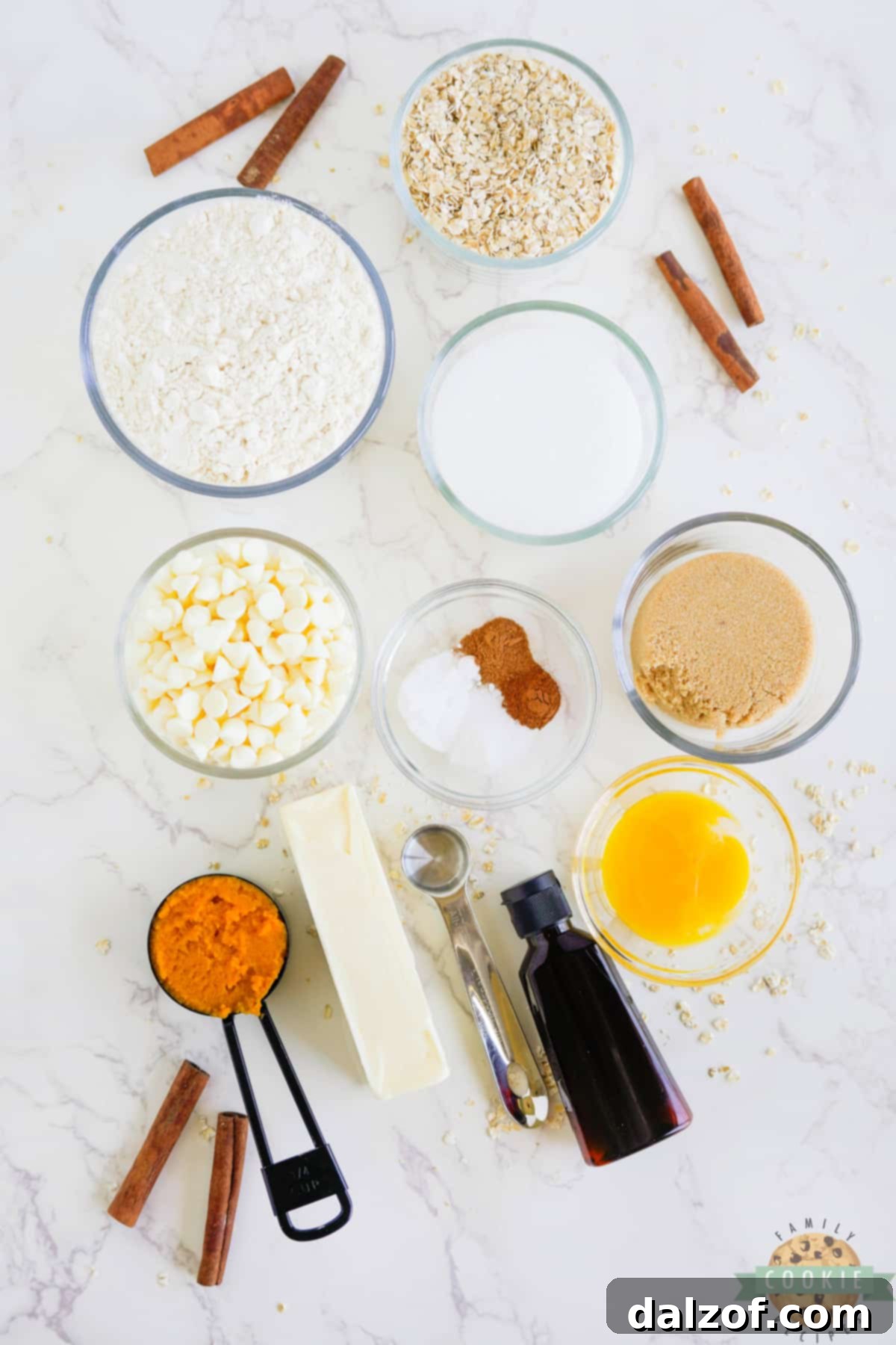 A collection of ingredients laid out, including pumpkin puree, spices, flour, oats, and white chocolate chips, for making pumpkin oatmeal cookies.