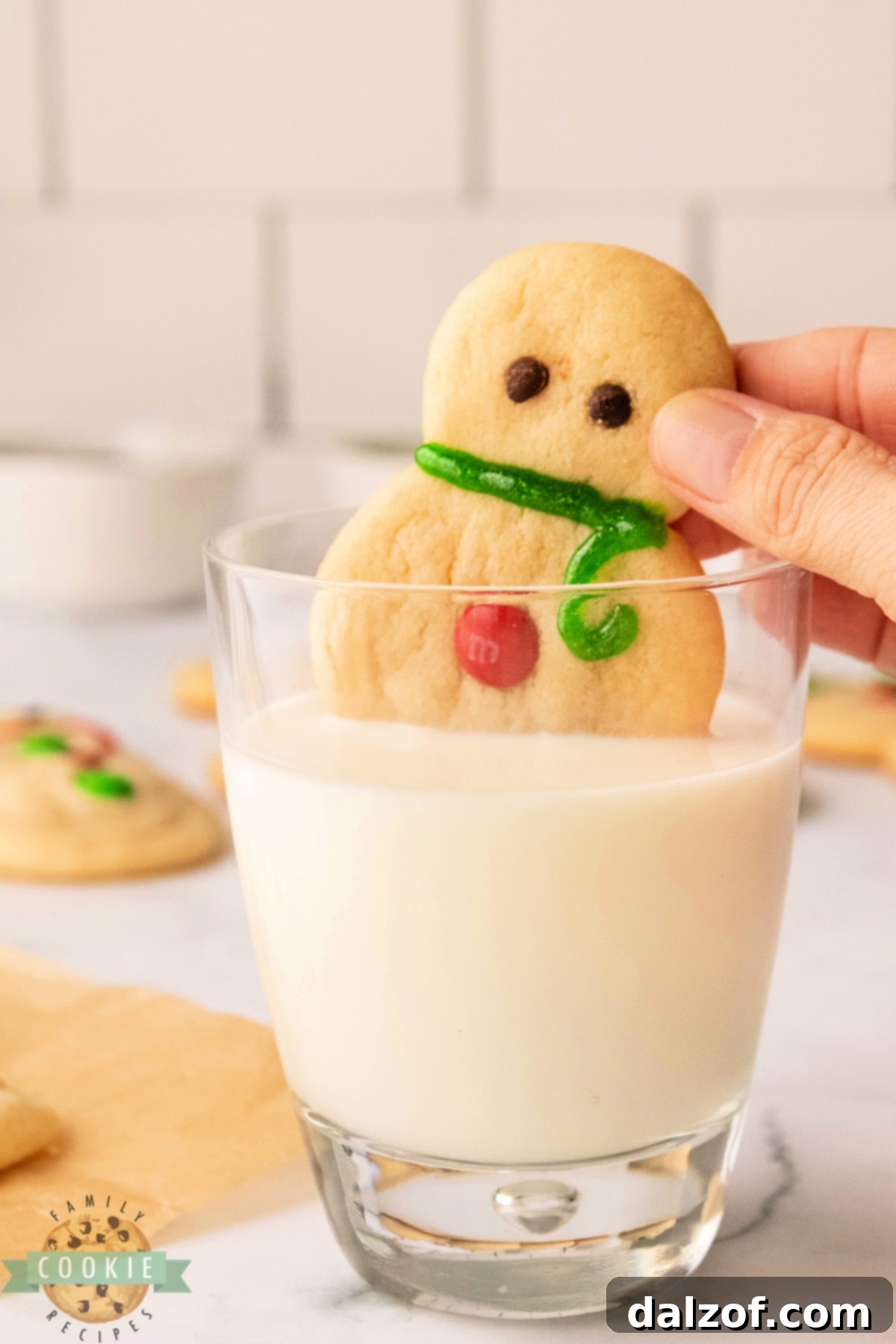 A freshly baked snowman sugar cookie being dipped into a glass of cold milk.