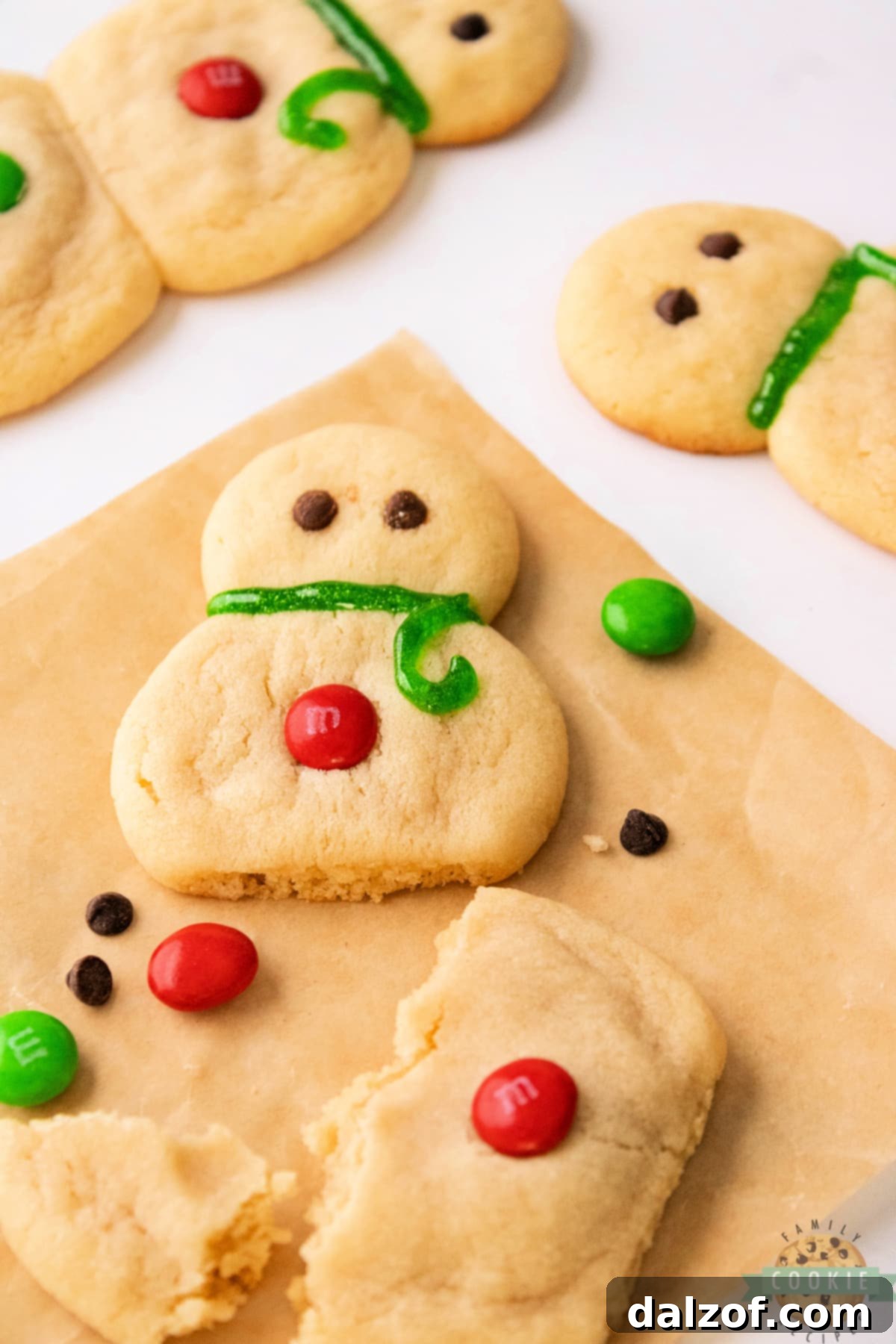 A single snowman sugar cookie artfully decorated with mini chocolate chip eyes, M&M buttons, and a red icing scarf.
