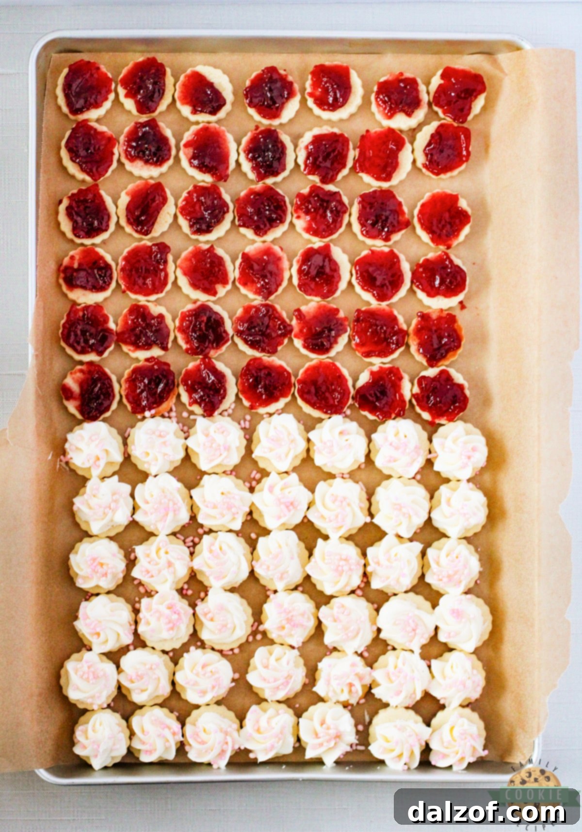 Filling empire cookies with raspberry jam and topping with buttercream frosting. 