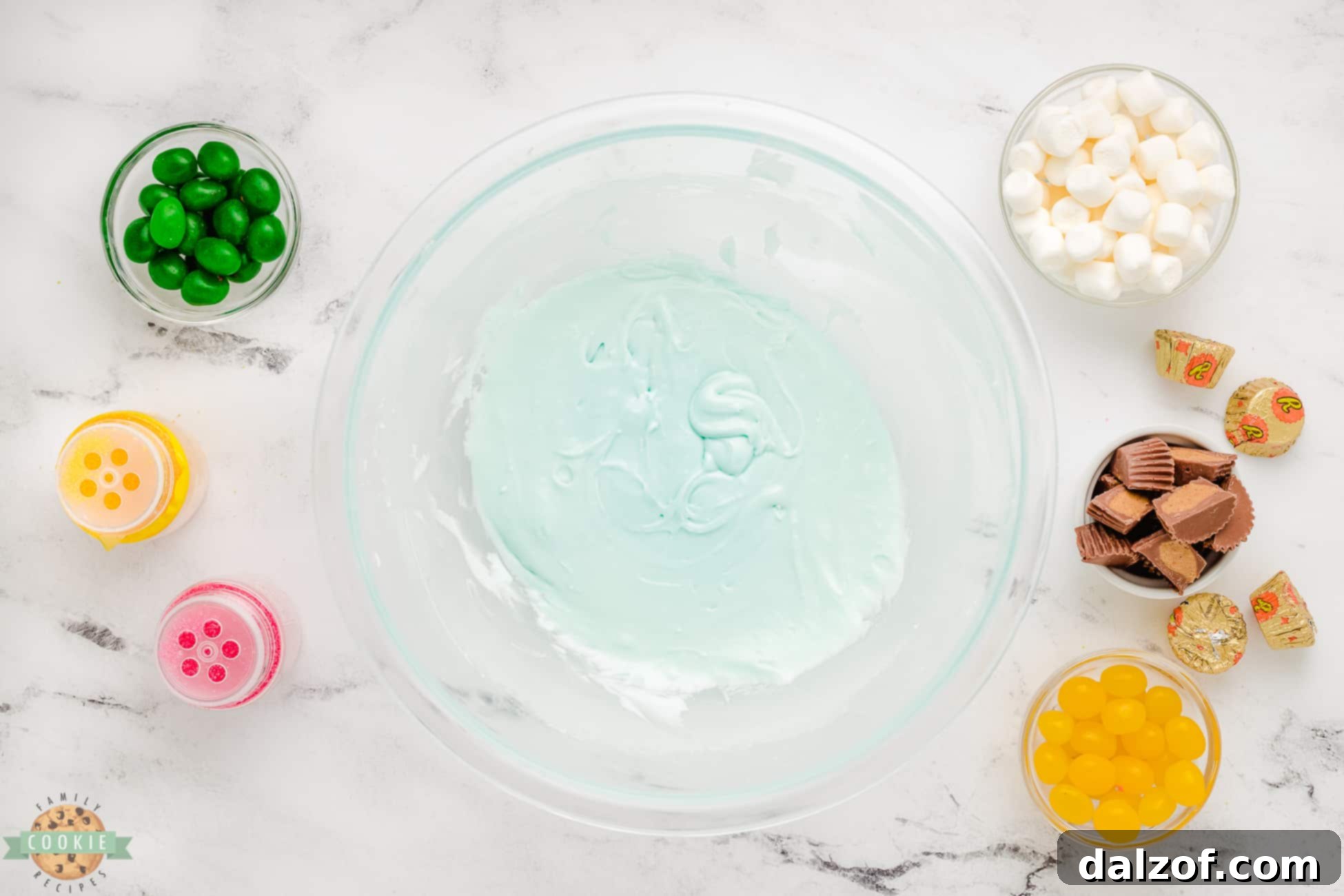 Close-up of a bowl filled with light blue frosting, ready to be spread onto sugar cookies, creating a perfect sky background for the flower decorations.