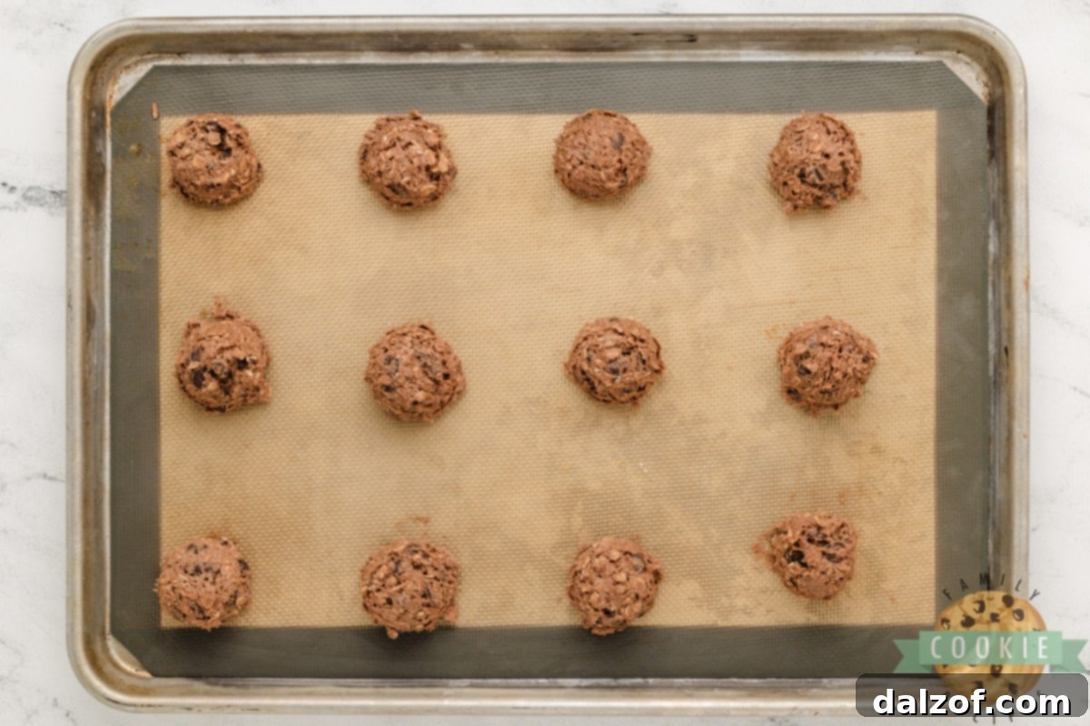 Scooped balls of double chocolate oatmeal cookie dough evenly spaced on a parchment-lined baking sheet, ready for the oven.