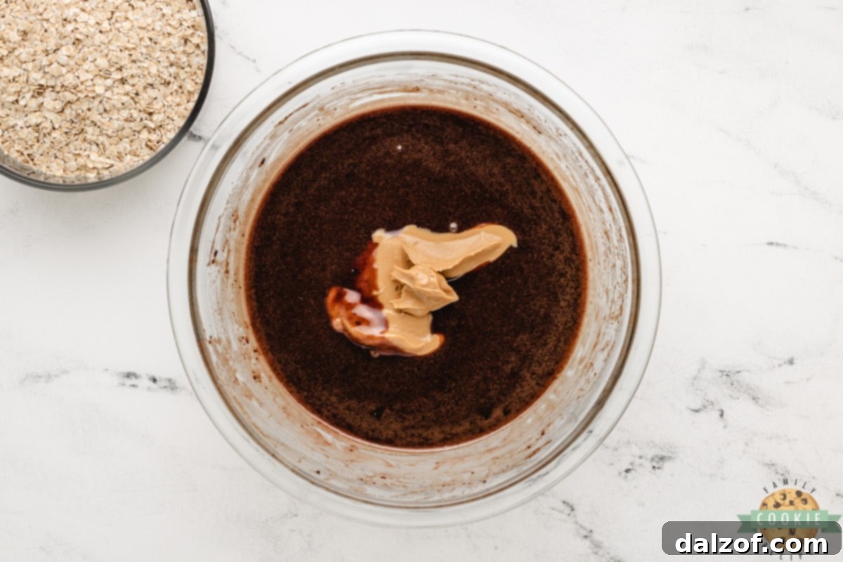 Adding creamy peanut butter to the warm chocolate mixture, preparing for the next step in making no-bake cookies.