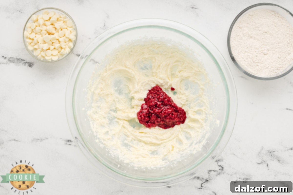 The vibrant frozen raspberry mixture being added to the creamy butter and sugar blend.