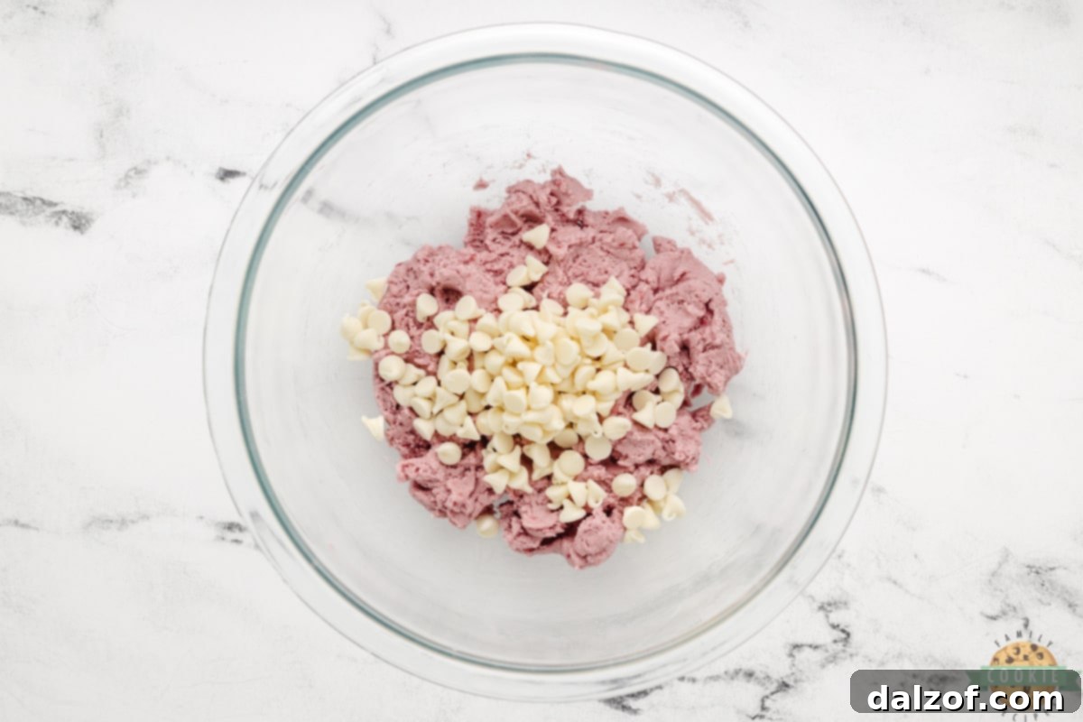 Folding luscious white chocolate chips into the pink raspberry cookie dough.