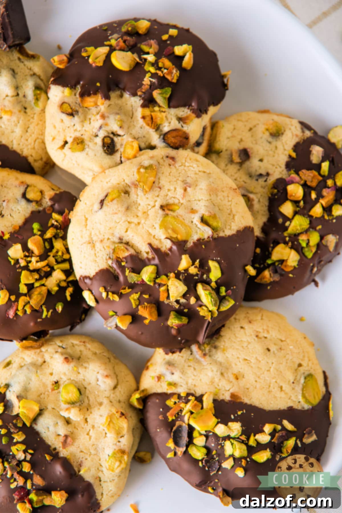 A close-up of a stack of Chocolate Dipped Pistachio Cookies, highlighting their soft texture and the generous chocolate coating.