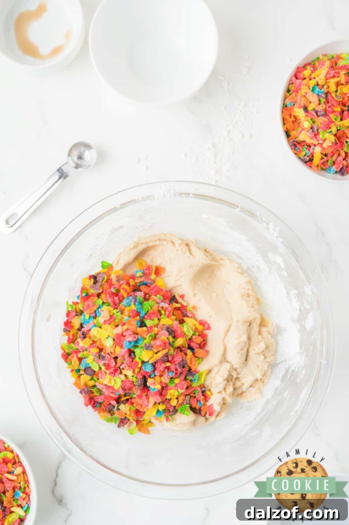 Gently folding Fruity Pebbles cereal into cookie dough with a spatula.