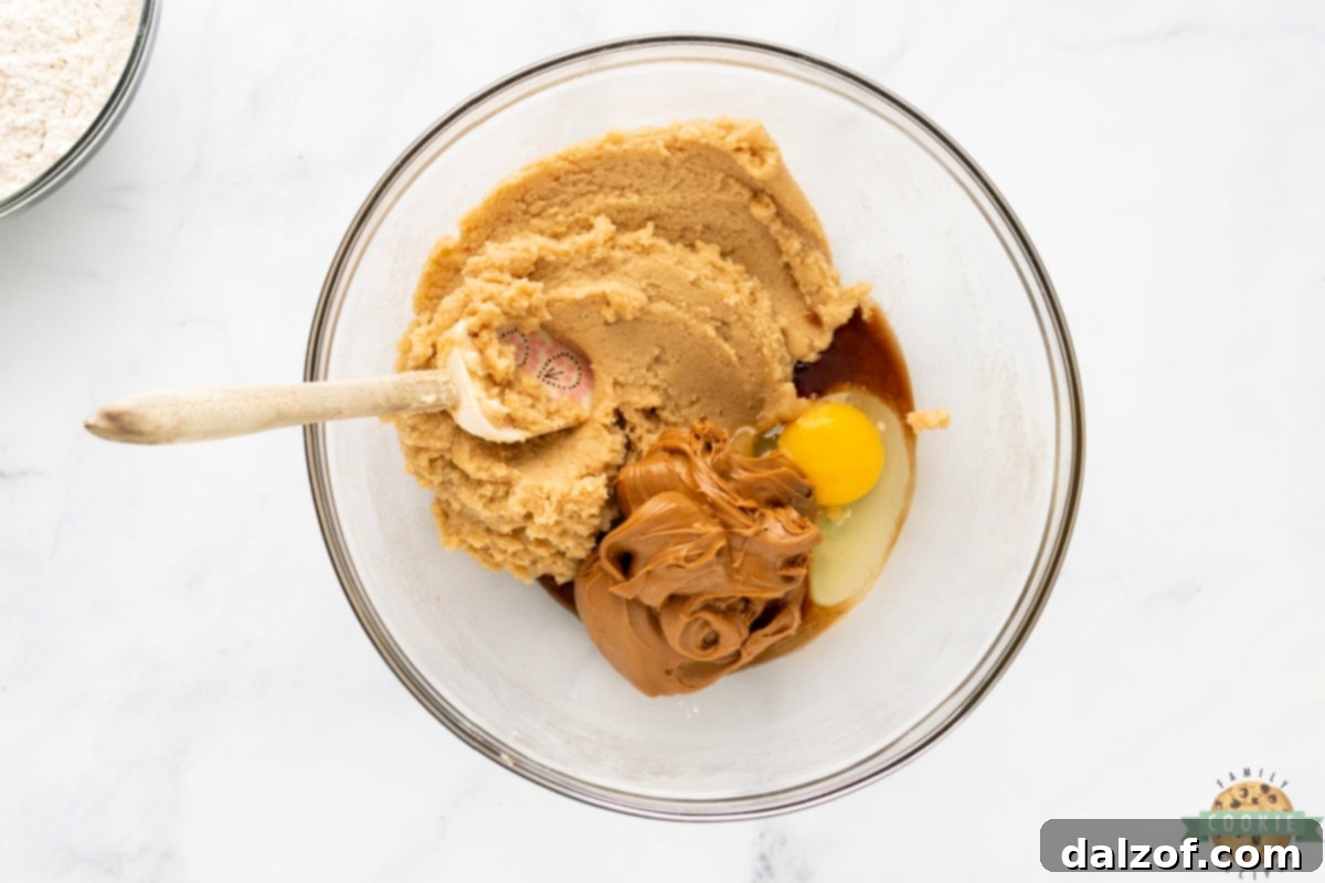 Egg, cookie butter, and vanilla extract being added to the creamed butter and sugar mixture.