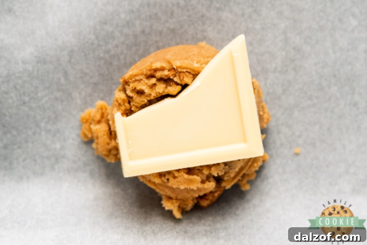 Process of adding a piece of white chocolate into the center of a cookie dough ball using a scoop.
