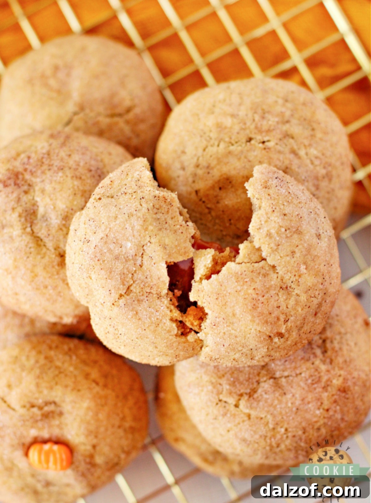 Close-up shot of an unwrapped soft caramel being gently pressed into the center of a pumpkin snickerdoodle cookie dough ball, ready to be fully encased.
