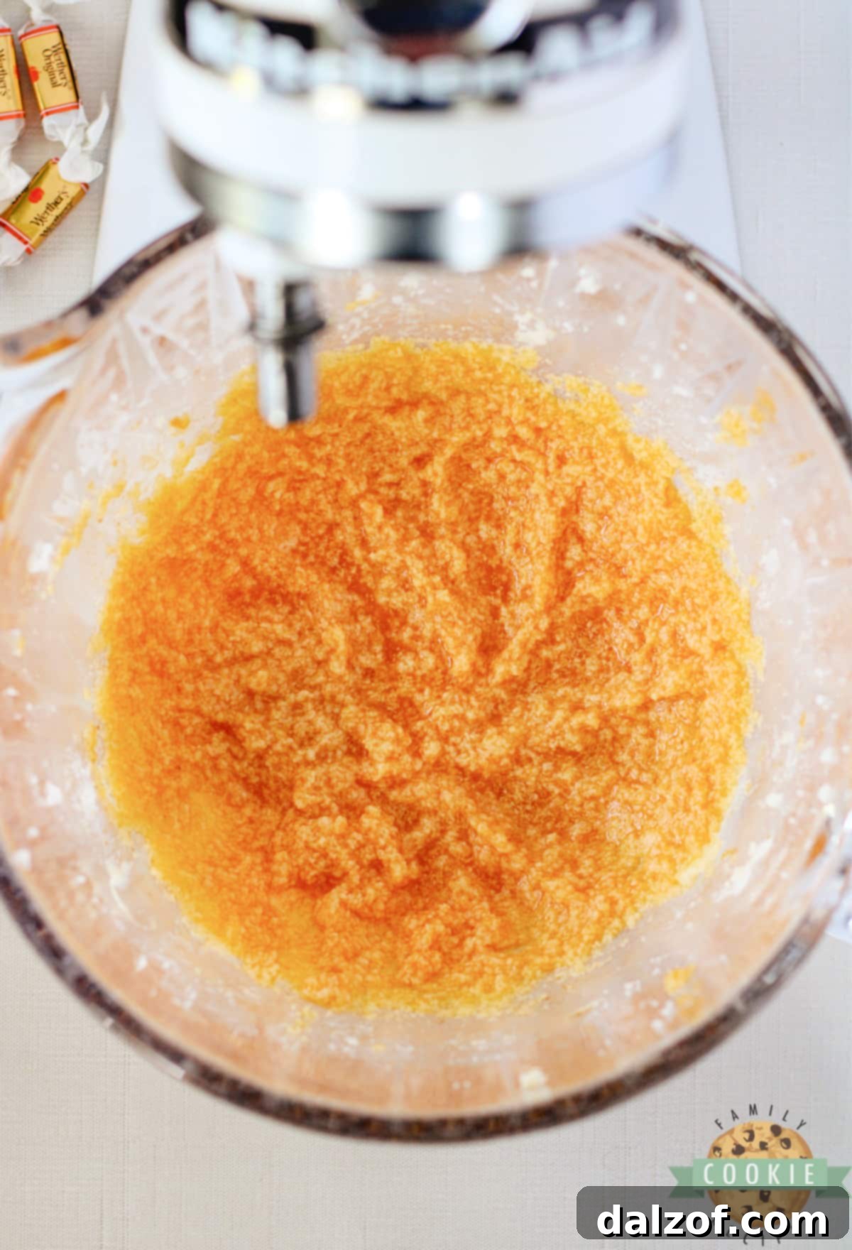 A large mixing bowl containing the creamed butter and sugar, with a raw egg, a splash of vanilla extract, and four tablespoons of canned pumpkin puree being added to the mixture.