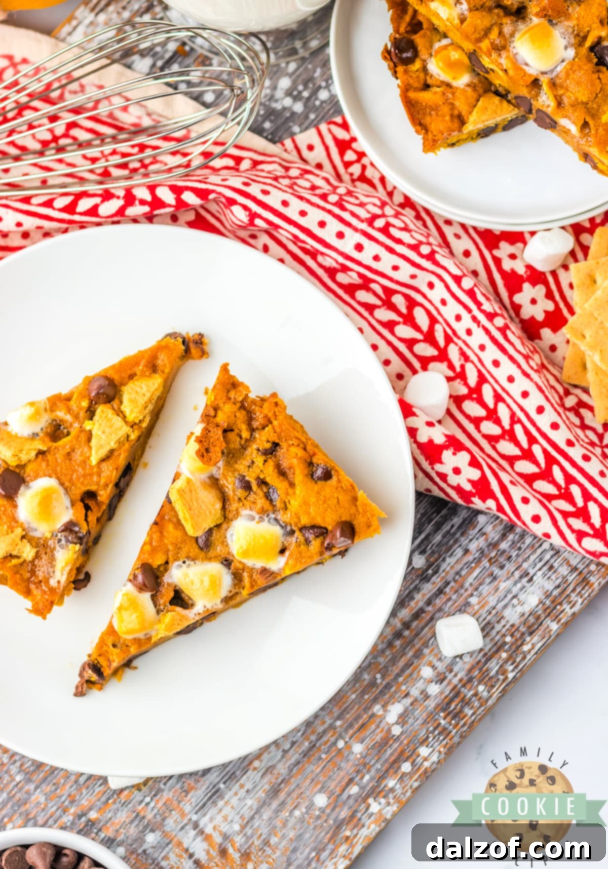 Ooey Gooey Pumpkin S'mores Cookie Cake 15 Multiple slices of Pumpkin S'mores Cookie Cake neatly arranged on a white platter, showcasing the golden crust, melted chocolate, and soft, pumpkin-flavored interior.
