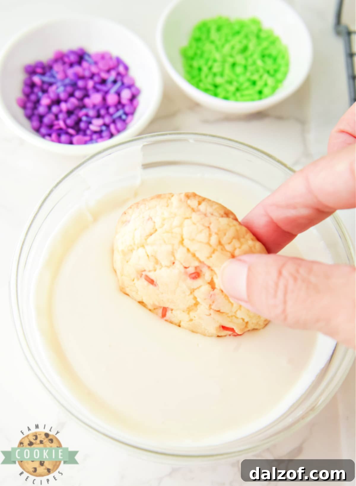 A baked cake mix cookie being dipped into a bowl of warm, melted vanilla frosting.
