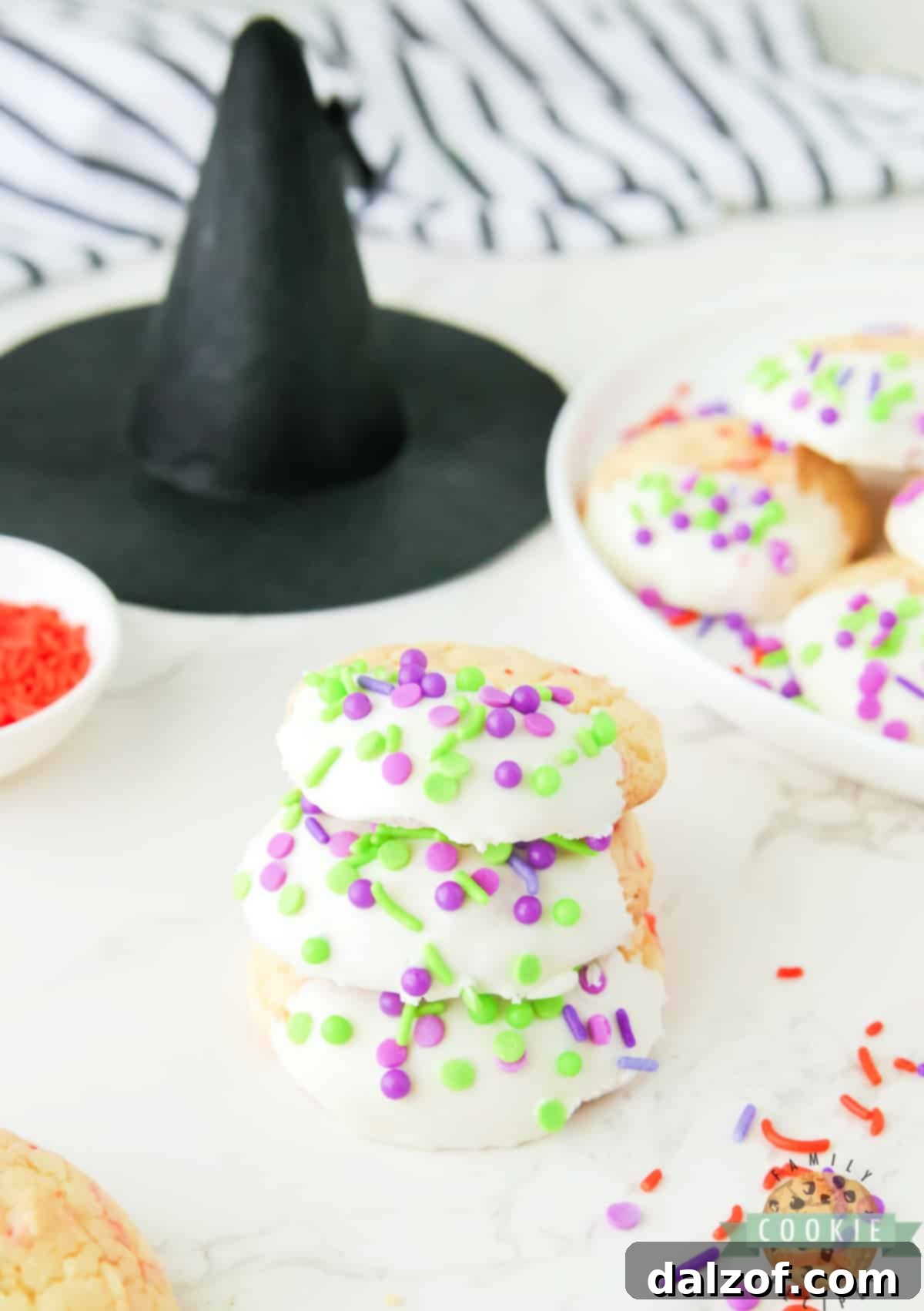 Freshly baked cake mix cookies, half-dipped in smooth vanilla frosting, ready for vibrant Halloween sprinkles.