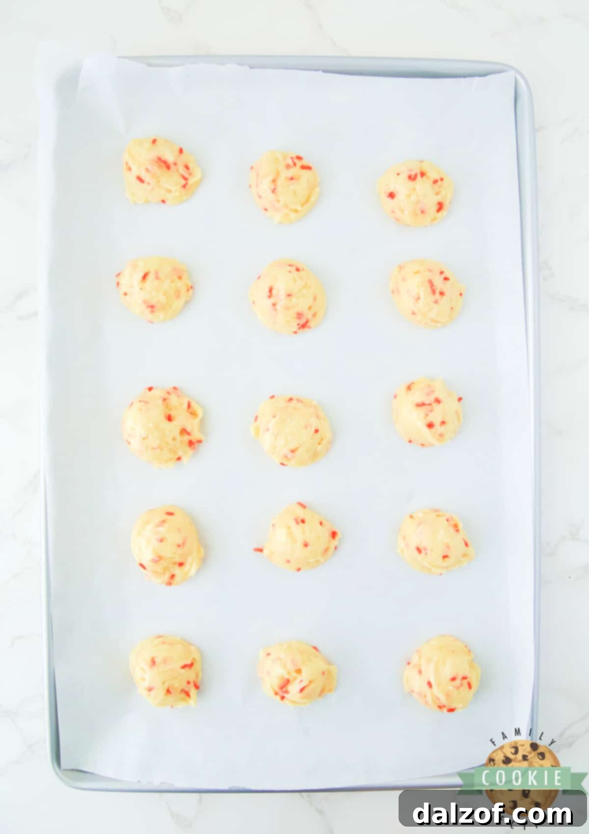 Neatly scooped balls of cake mix cookie dough, studded with sprinkles, arranged on a parchment-lined baking sheet.