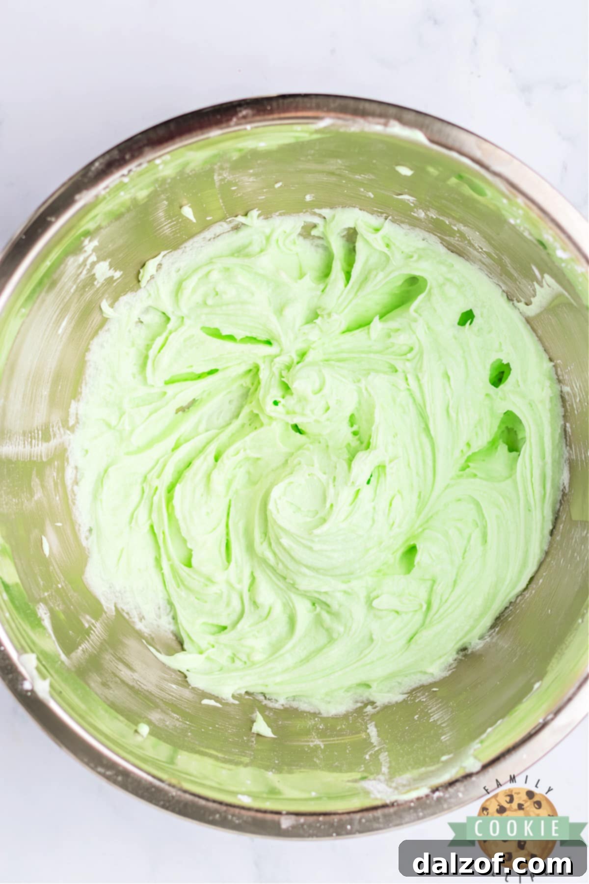 Smooth and creamy mint frosting, bright green in color, in a mixing bowl after being beaten with an electric mixer.