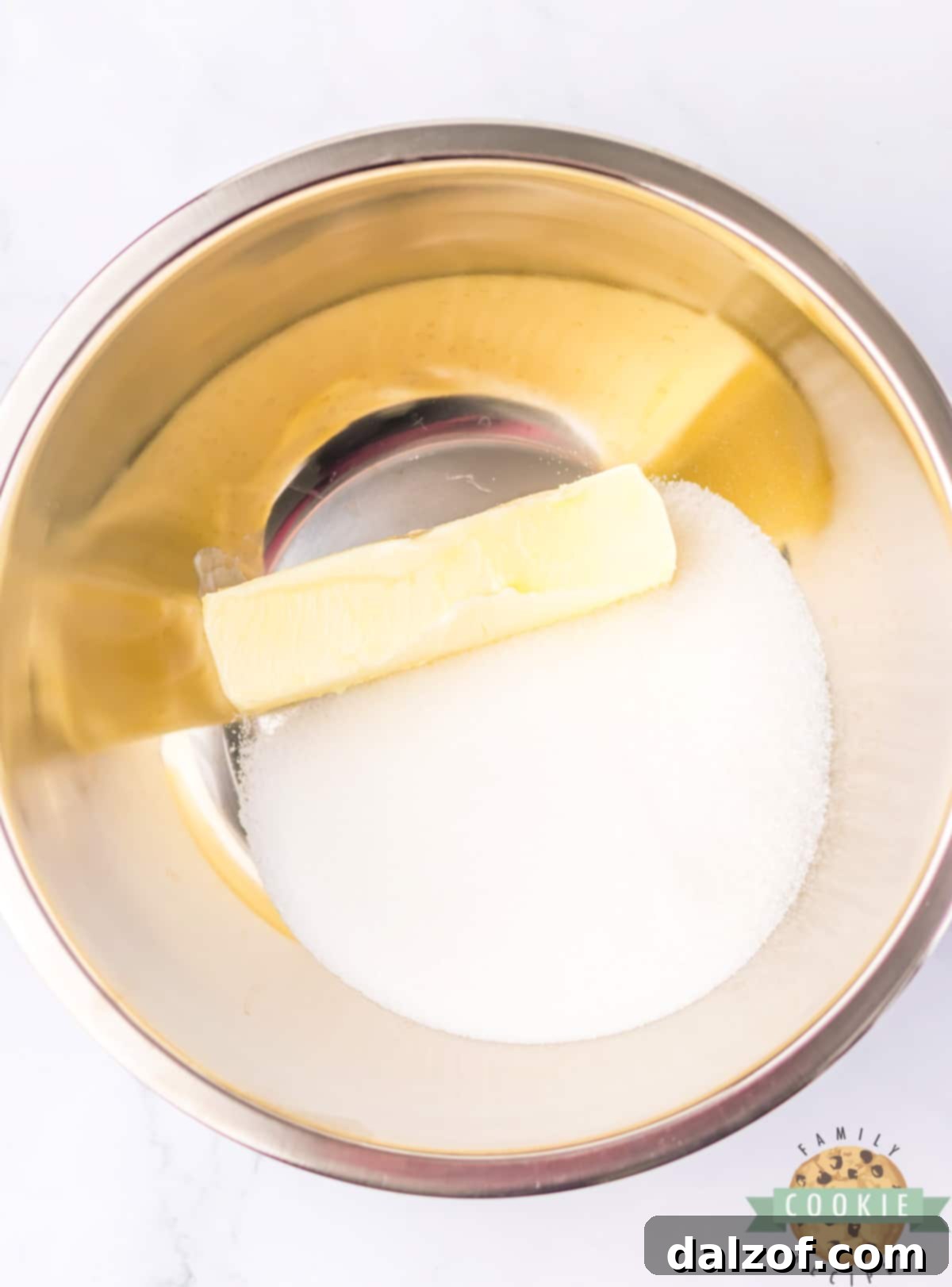 Softened butter and granulated sugar being creamed together in a mixing bowl with an electric mixer, forming a light and fluffy mixture.