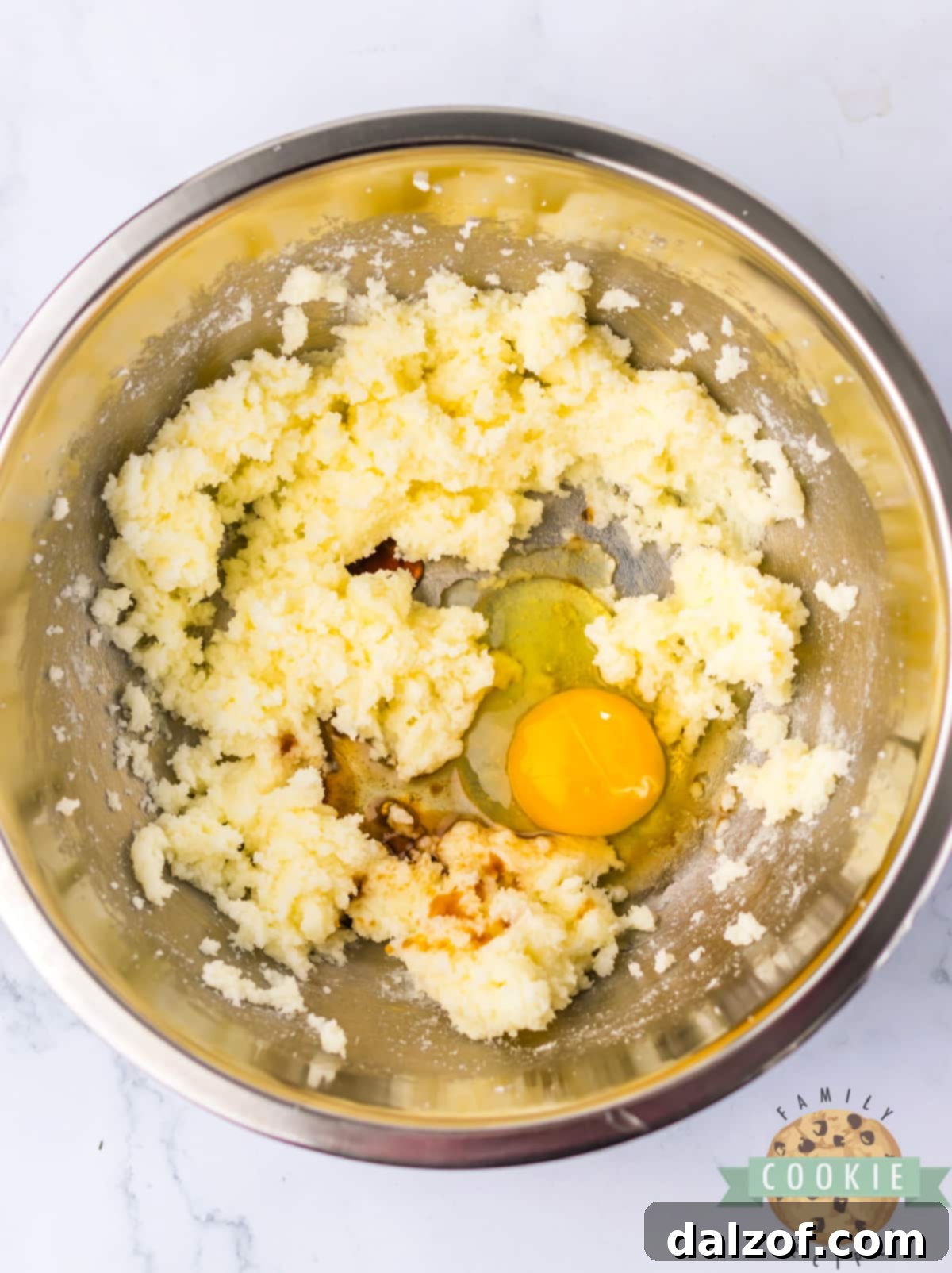 Vanilla extract and a large egg being added to the creamed butter and sugar mixture in a bowl, ready for further mixing.