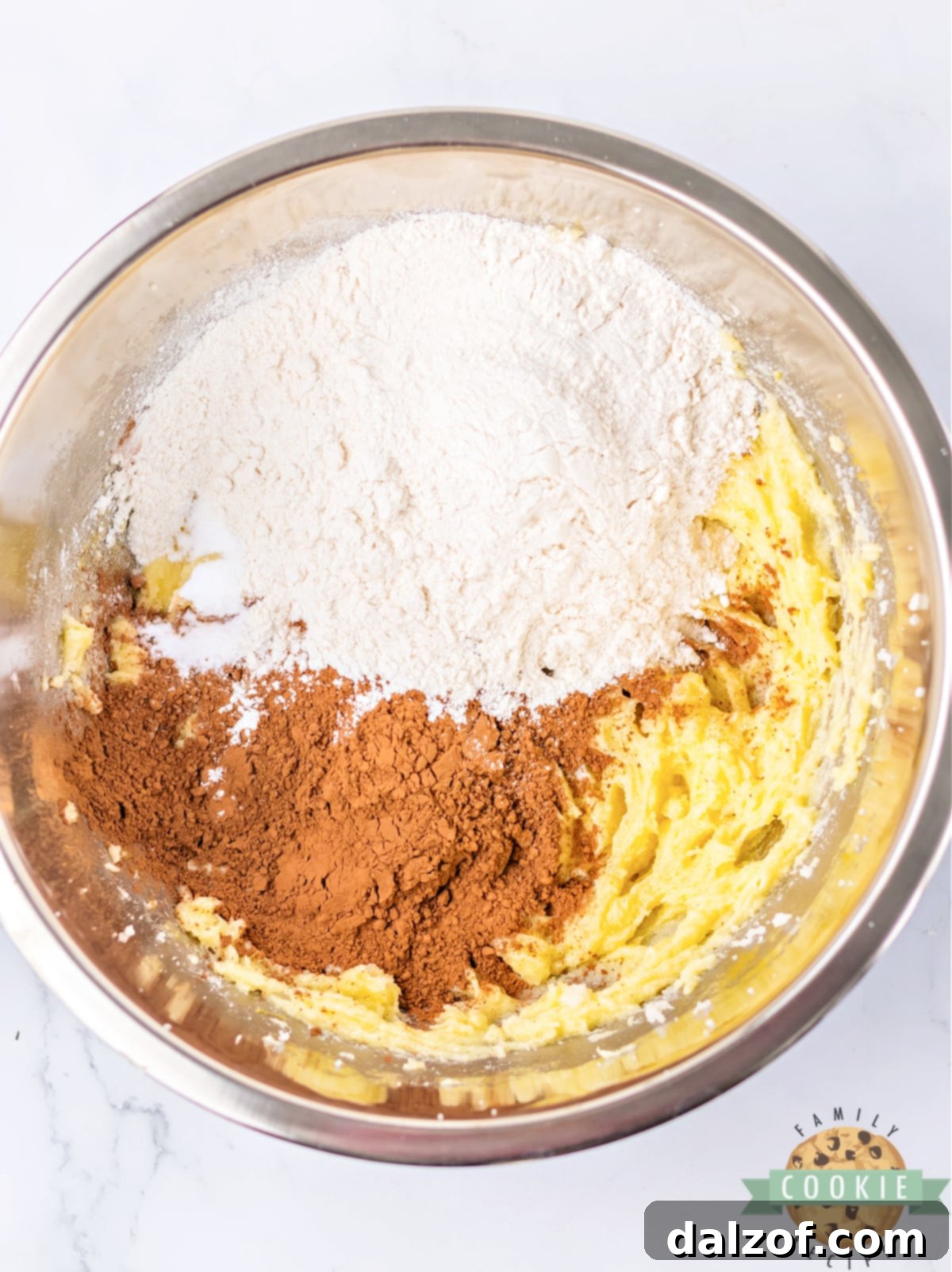 All-purpose flour, cocoa powder, baking soda, and salt added to the wet ingredients in a mixing bowl, ready to be combined into cookie dough.