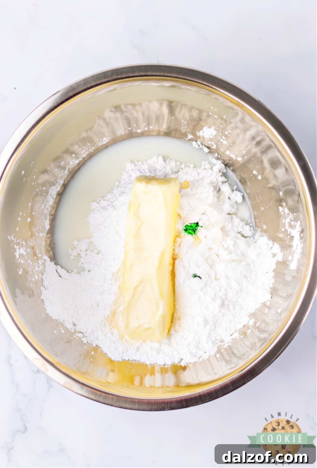 Ingredients for mint frosting: butter, powdered sugar, milk, peppermint extract, and green food coloring in a bowl.