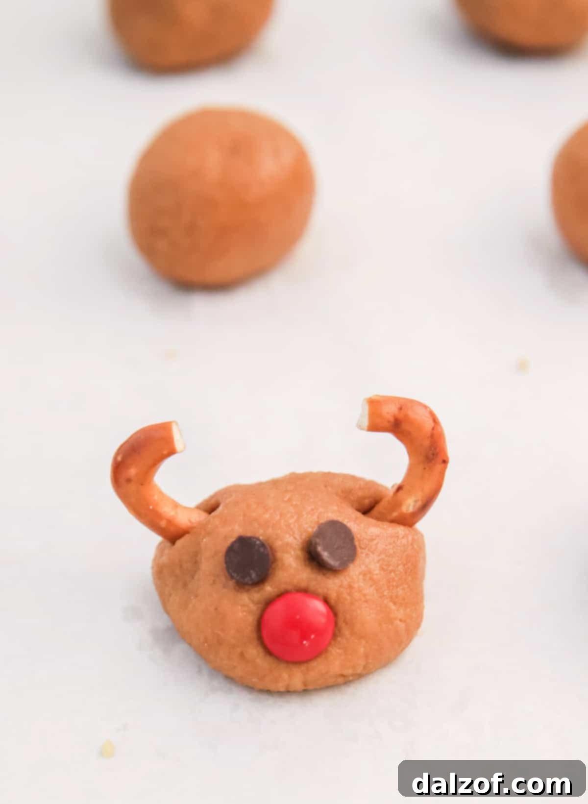 Rudolph's Red-Nosed Cookie Butter Delights 8 Decorating no-bake Rudolph Cookie Butter Balls with mini chocolate chip eyes, a red M&M nose, and pretzel antlers.
