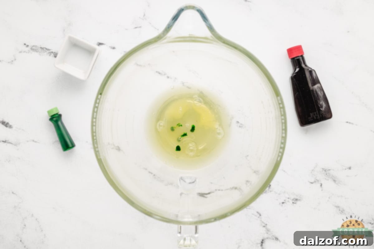 Individual ingredients including egg white, salt, cream of tartar, peppermint extract, and green food coloring, ready to be combined.