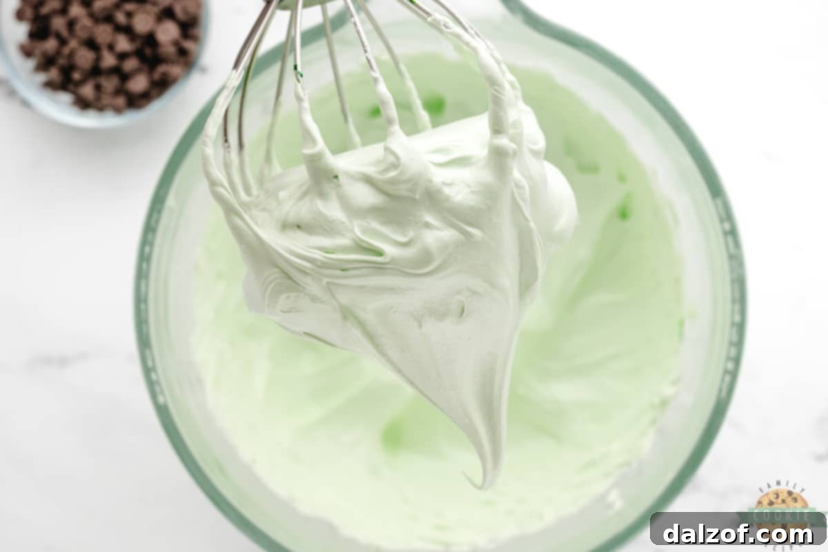 Egg whites, salt, cream of tartar, mint extract, and food coloring whipped to soft peaks in a large mixing bowl.