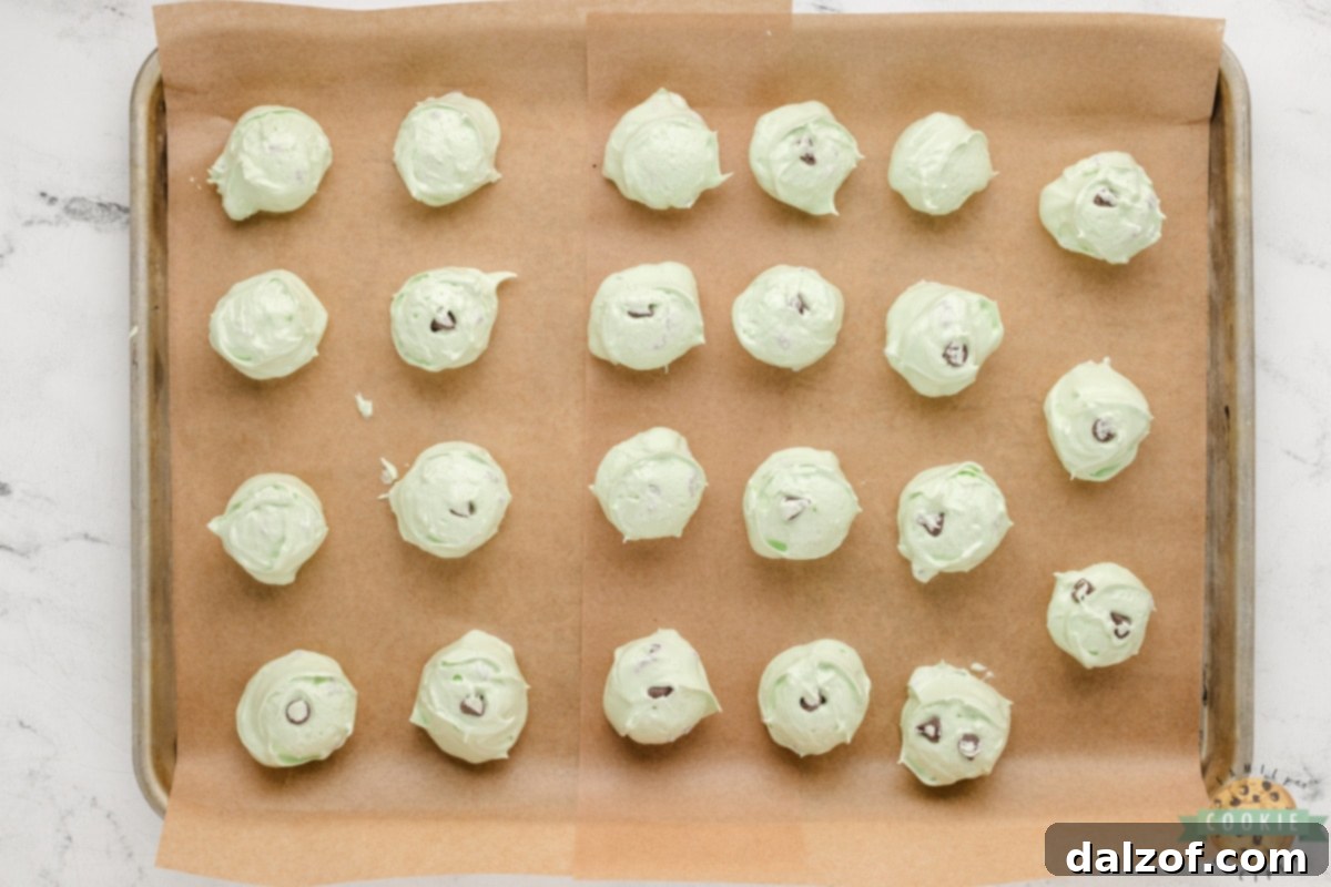 Mini chocolate chips being gently folded into the mint-flavored meringue mixture with a spatula.