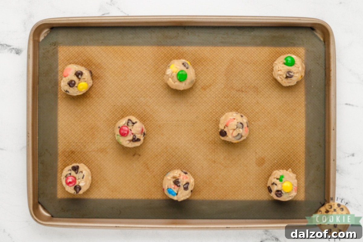Scooping tablespoon-sized balls of 5-Ingredient Monster Cookie dough onto a prepared cookie sheet before baking.